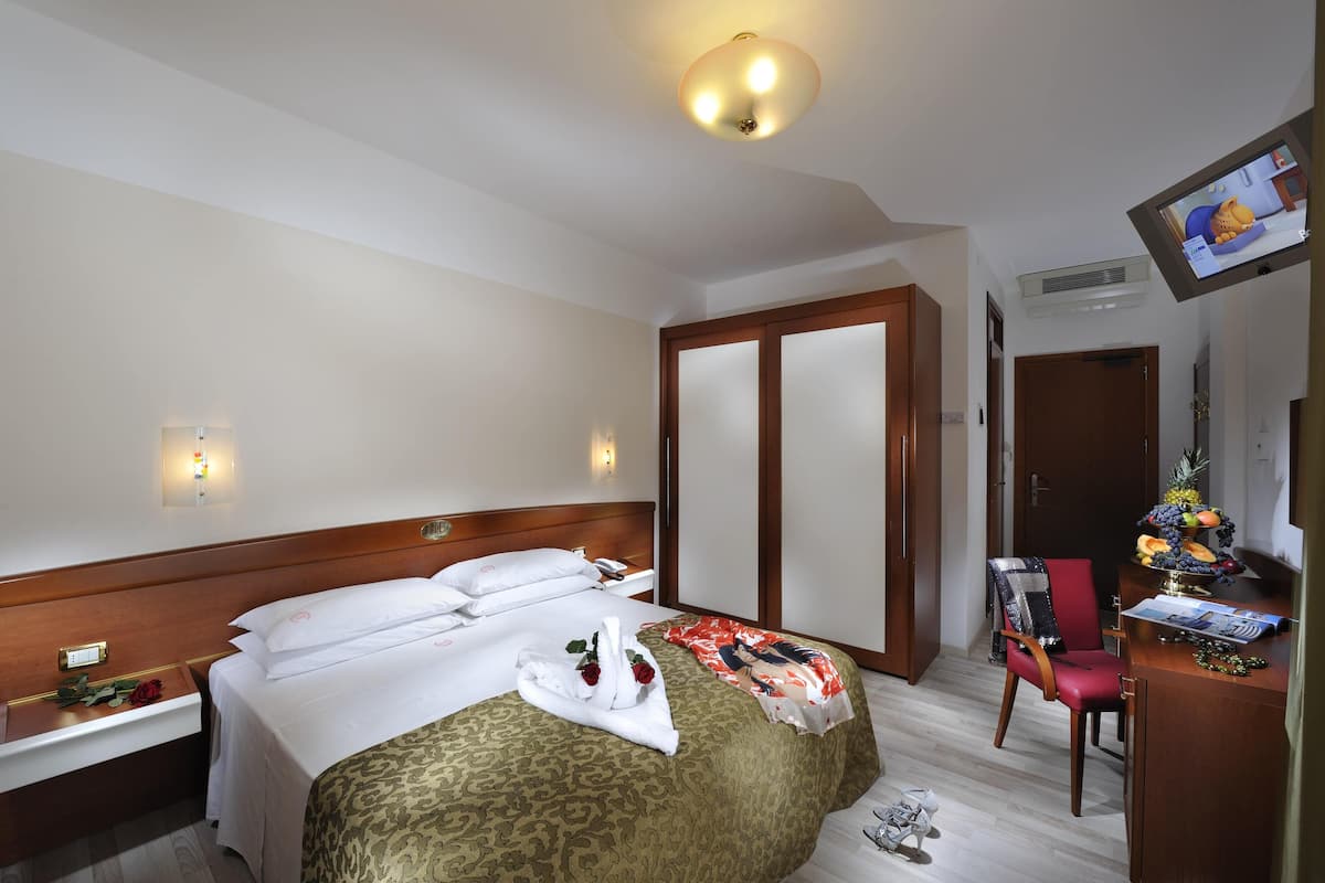 Een hotelkamer met een bed, nachtkastje, televisie, bureau en stoel.