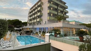 Ένα σύγχρονο ξενοδοχείο με πισίνα στην ταράτσα, πολλά μπαλκόνια και εξωτερικούς χώρους για καθιστικό.