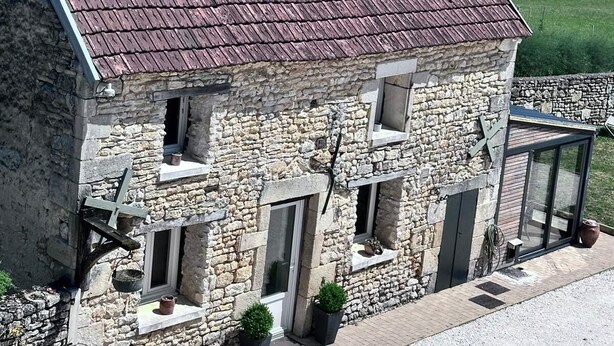 Un bâtiment en pierre doté d’un toit en pente, de nombreuses fenêtres et d’un petit porche agrémenté de plantes en pot.