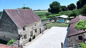 Un bâtiment en pierre doté d’un toit en pente, d’un espace extérieur abrité avec des sièges et d’une vue sur une piscine.
