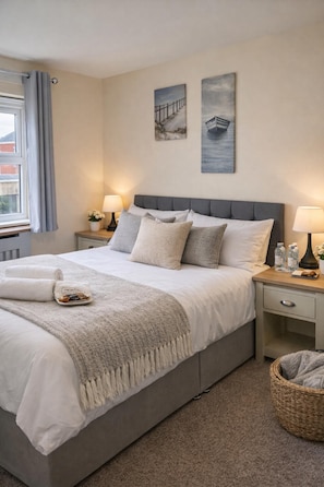 A neatly made bed with a grey headboard, a bedside table with a lamp, and a small basket on the floor.