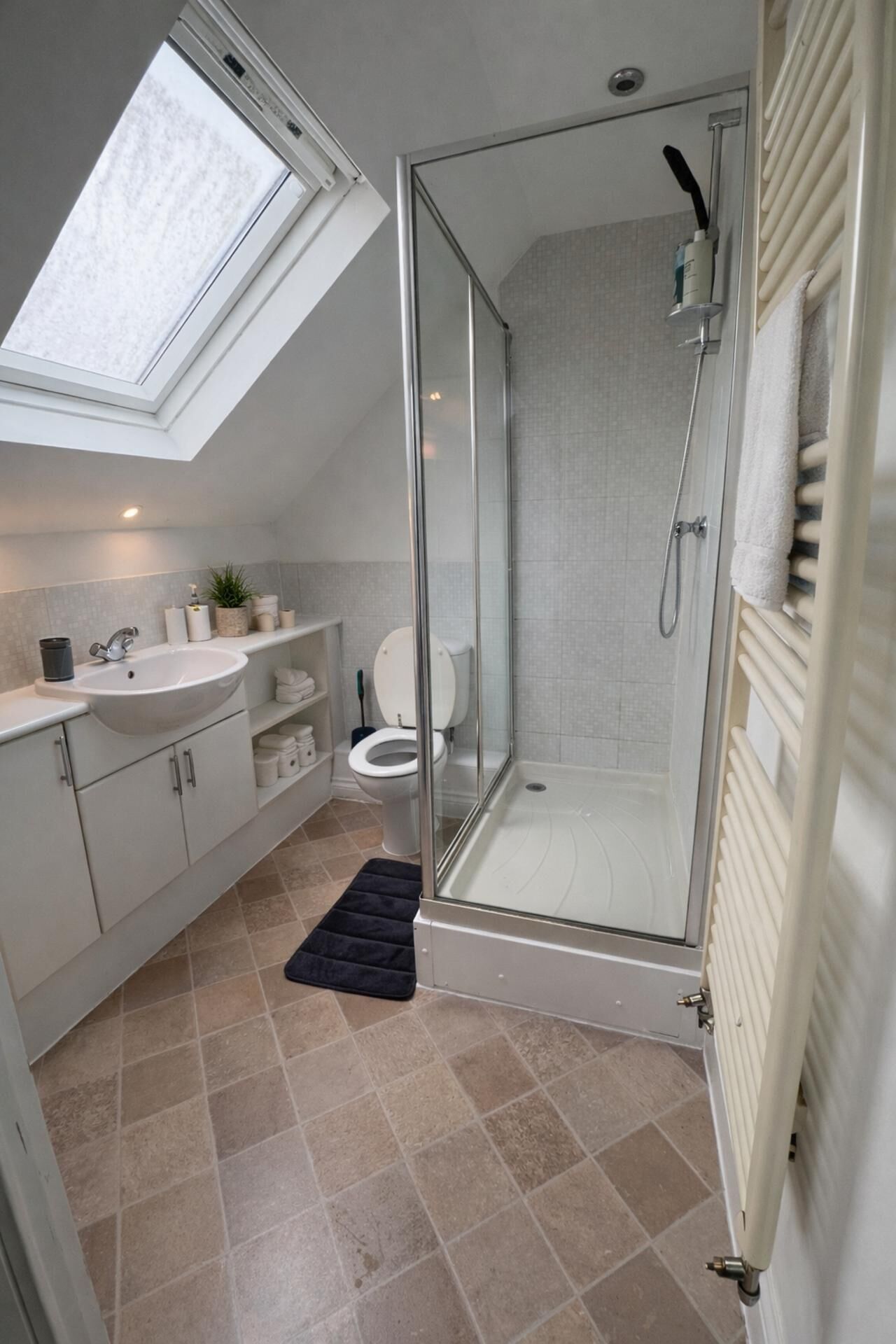 A modern bathroom with a skylight, a glass-enclosed shower, a toilet, and a sink.