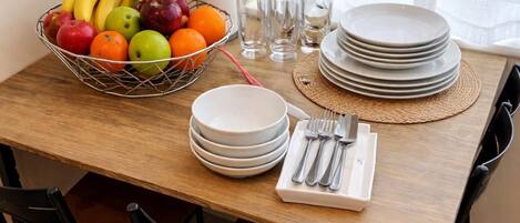 Una mesa de comedor servida con platos, cubiertos y una cesta de frutas.