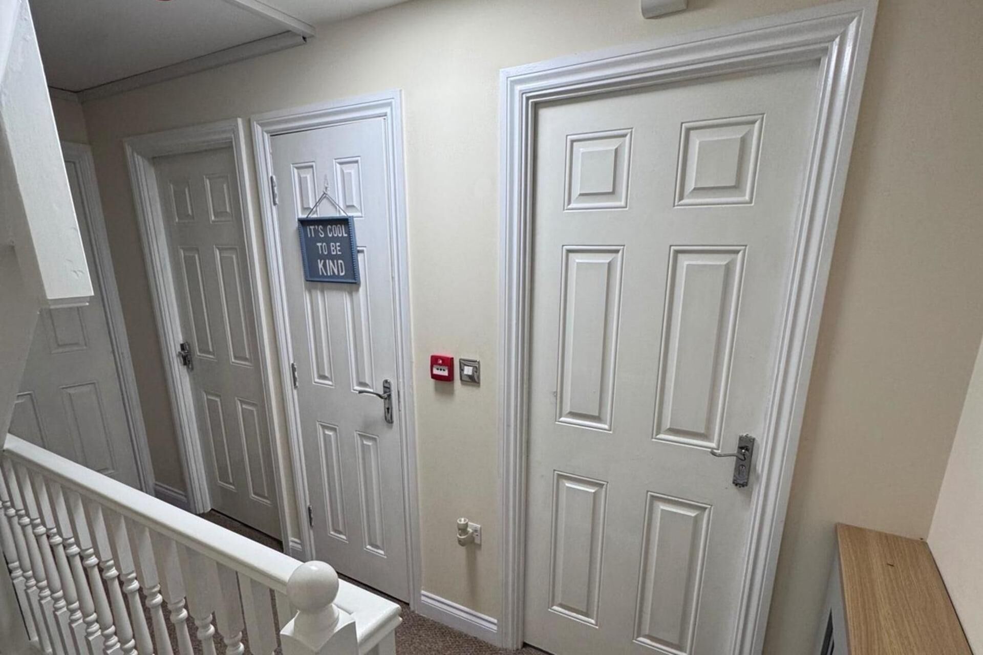 A hallway with white doors, a sign on one door, and a red electrical outlet.