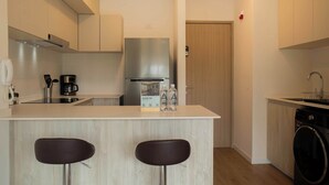 A modern kitchen with a central island, two bar stools, a coffee machine, a stainless steel refrigerator, and a washing machine. - w* | Amazing & Cozy 2BR w/ Balcony in San Isidro (Lima)