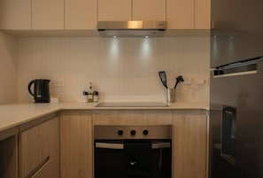 A modern kitchen with wooden cabinets, a built-in oven, a stainless steel refrigerator, and a coffee maker.