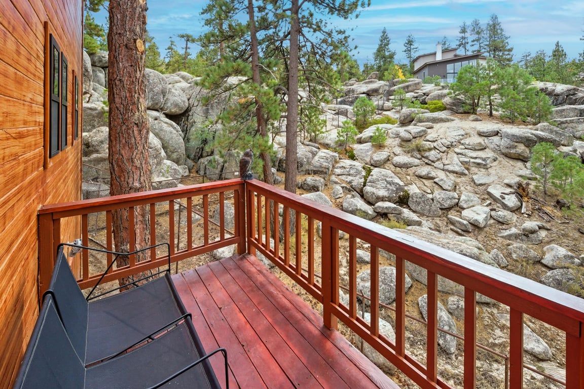 A wooden cabin with a deck, surrounded by rocks and trees.