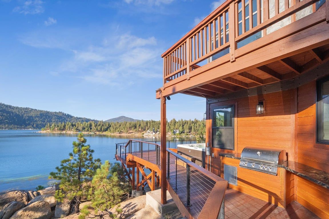 Une cabane en bois dotée d’une terrasse offrant une vue sur un lac, d’un barbecue et d’un panorama sur la forêt environnante.
