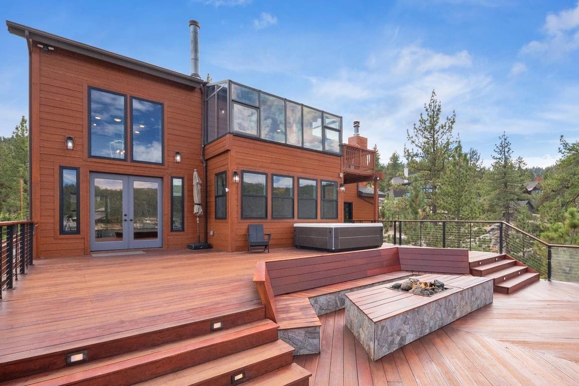 A modern two-story house with a deck, large windows, and a fire pit area.