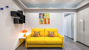 A bright yellow sofa with colorful cushions, a small table with a lamp, and a wall-mounted artwork above. - Pop House in the Heart of Sanita by Wonderful Italy (Naples)