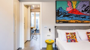 A modern hotel room with a bed, colorful pillows, a yellow stool, and a vibrant painting on the wall. - Pop House in the Heart of Sanita by Wonderful Italy (Naples)