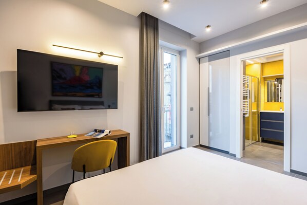 Une chambre d’hôtel moderne équipée d’un lit, d’un bureau, d’une chaise, d’une télévision et offrant une vue sur l’extérieur.