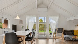 A spacious room with a high ceiling, a dining area with a table and chairs, a sofa, and a view of the outdoors.