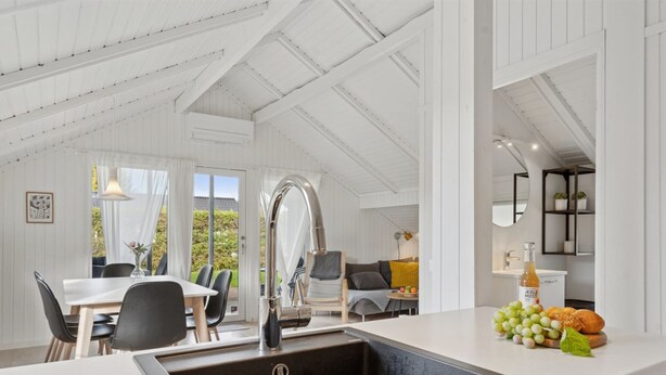 A modern kitchen with a large island, a dining area with a table and chairs, and a view of the outdoors through large windows.