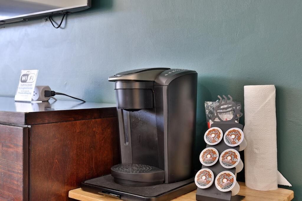 A coffee machine with a drip tray, a tissue roll, and a stack of donut containers on a wooden counter.