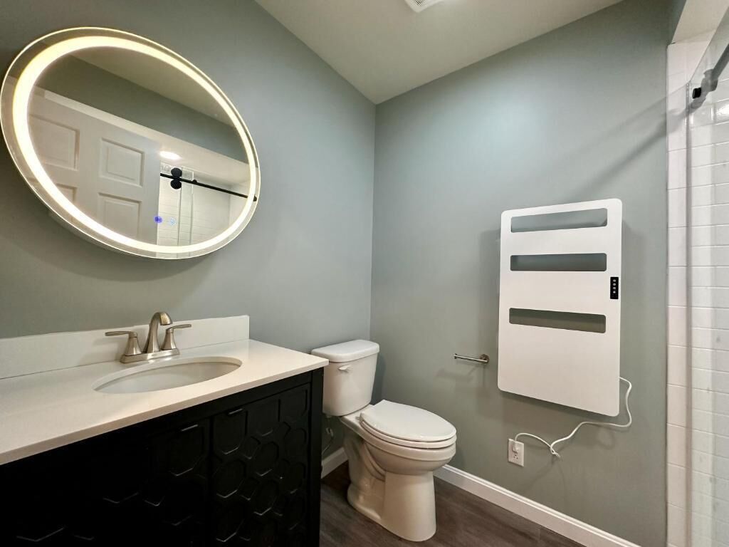 A bathroom with a round mirror, a sink, a toilet, and a wall-mounted air purifier.