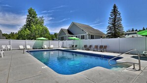 A swimming pool with lounge chairs and umbrellas, surrounded by a white fence and tall trees.