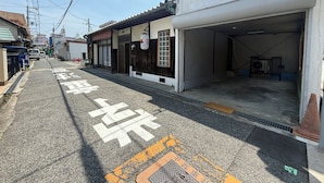 Una calle estrecha con un edificio a la derecha que tiene una puerta de garaje abierta. Hay coches estacionados a la izquierda de la calle.