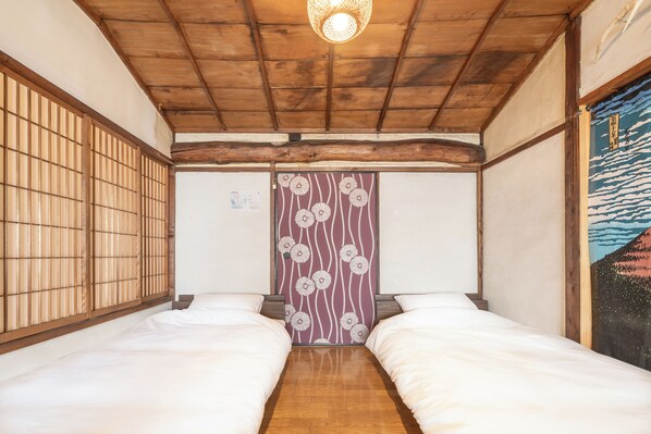 A traditional Japanese room with two beds, wooden flooring, a tatami mat entrance, and a shoji screen with floral patterns.