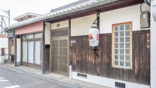 Edificio japonés tradicional con fachada de madera, tejado de tejas y un gran ventanal con diseño de cuadrícula.