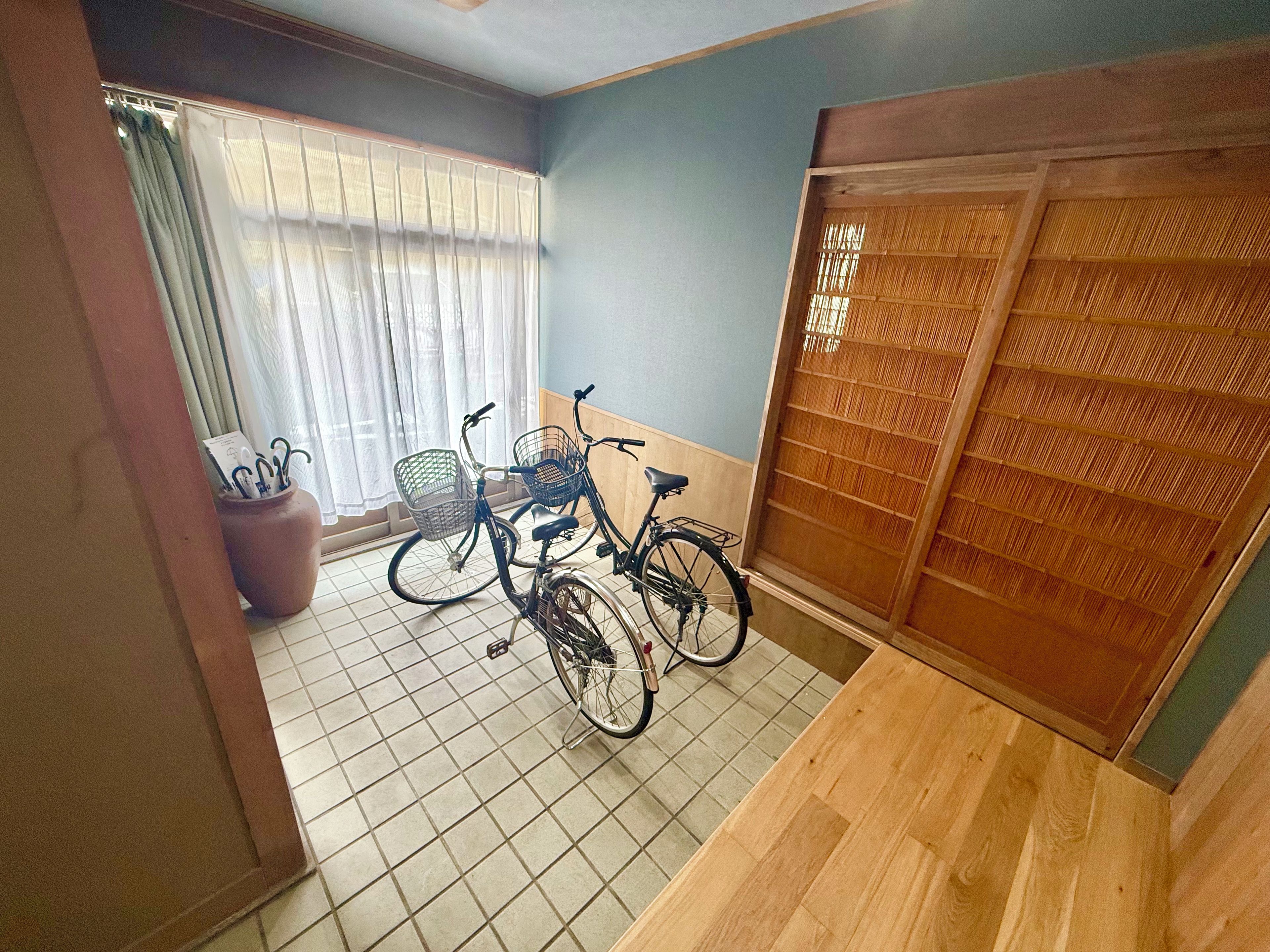 A room with a tiled floor, a wooden door with a decorative panel, and two bicycles with baskets.
