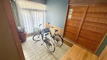 A room with a tiled floor, a wooden door with a decorative panel, and two bicycles with baskets.