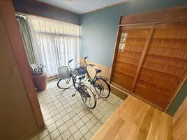 Una habitación con piso de baldosas, una puerta de madera con panel decorativo, y dos bicicletas con cestas.
