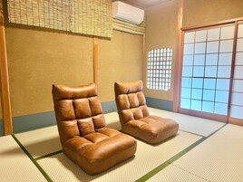 Un espacio tradicional con esteras de tatami, dos sillones de cuero marrón y un celosía de papel.