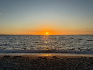 A beach at sunset with waves gently lapping the shore. - Sanada Maru (Kaizuka)