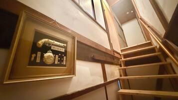 A framed display with a clock and other items on a wall, a wooden staircase with a handrail, and a window above.