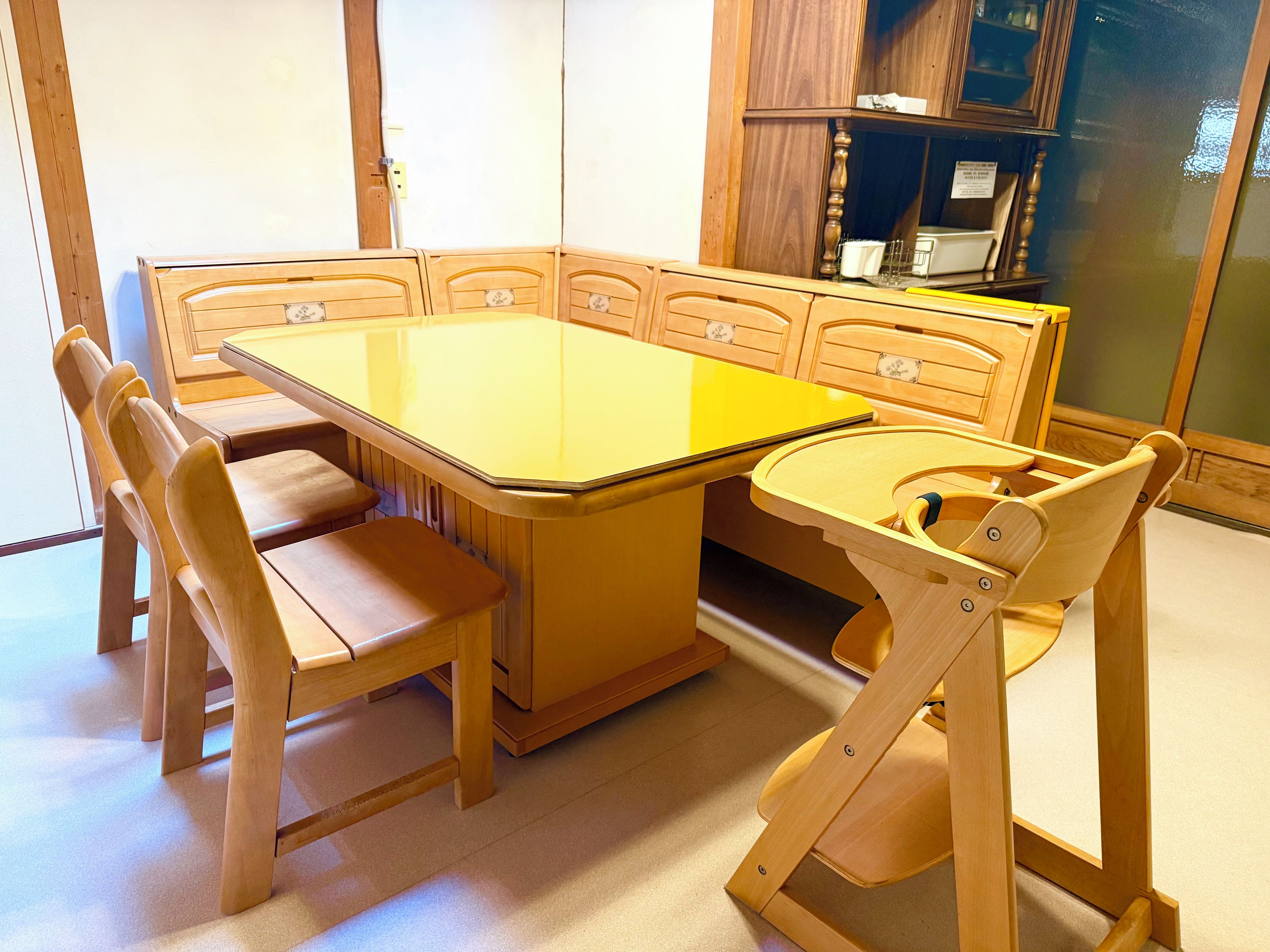 A dining area with a large rectangular table, six wooden chairs, and a cabinet with glass doors in the background.