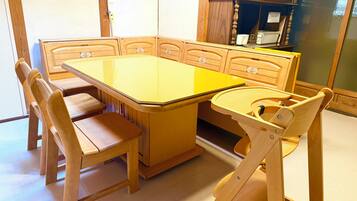 A dining area with a large rectangular table, six wooden chairs, and a cabinet with glass doors in the background.