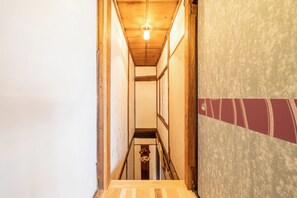 A narrow hallway with wooden walls and a wooden floor, leading to a room with a red and white patterned wall.