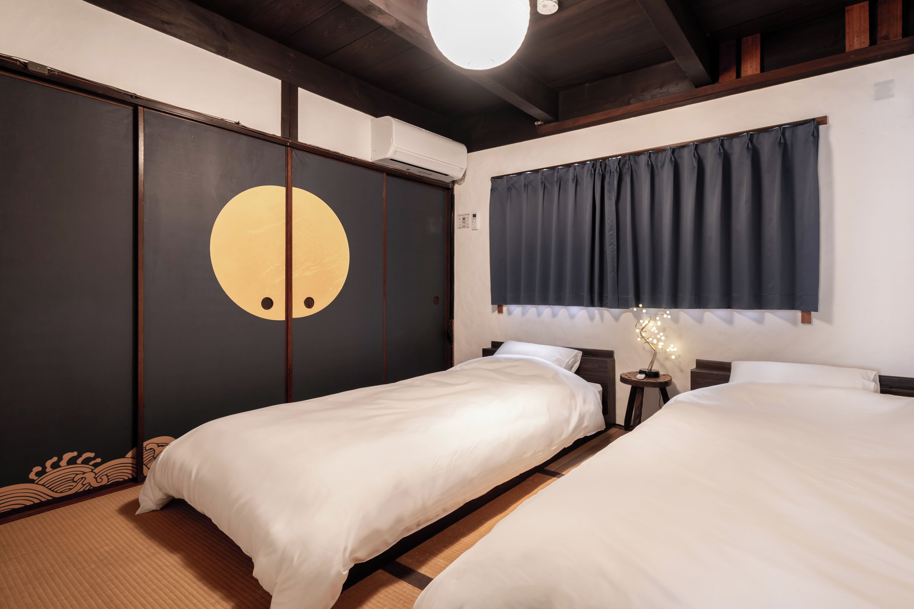 A hotel room with two beds, a large circular design on the wall, a ceiling fan, and a window with curtains.