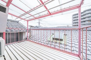 A balcony with a tiled roof, a red railing, and a view of a residential building. - Sanada Maru (Kaizuka)