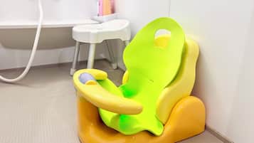 A child’s potty chair in a bathroom with a white sink and a white toilet in the background.
