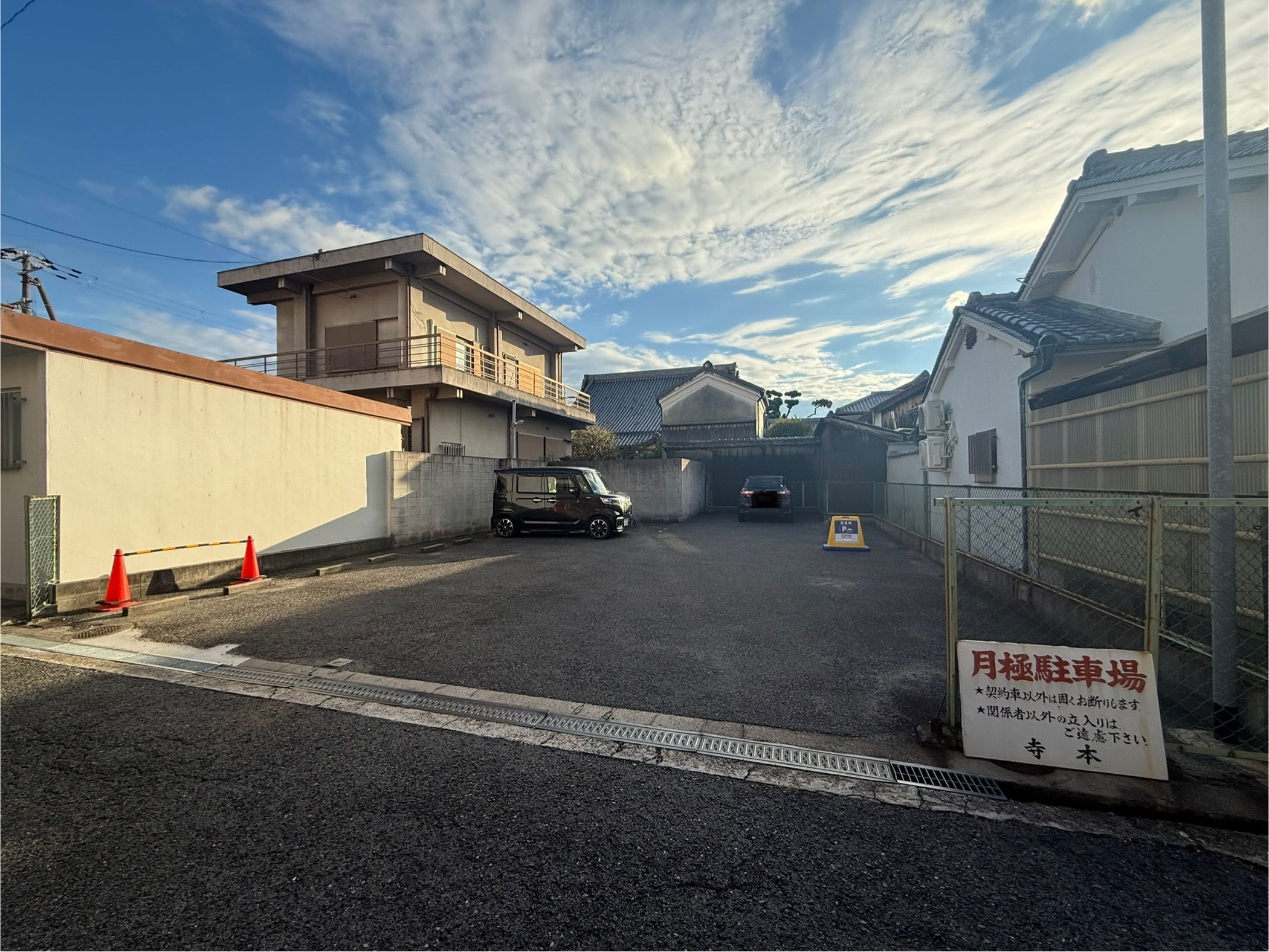 A parking area with a car and a signboard, surrounded by buildings.