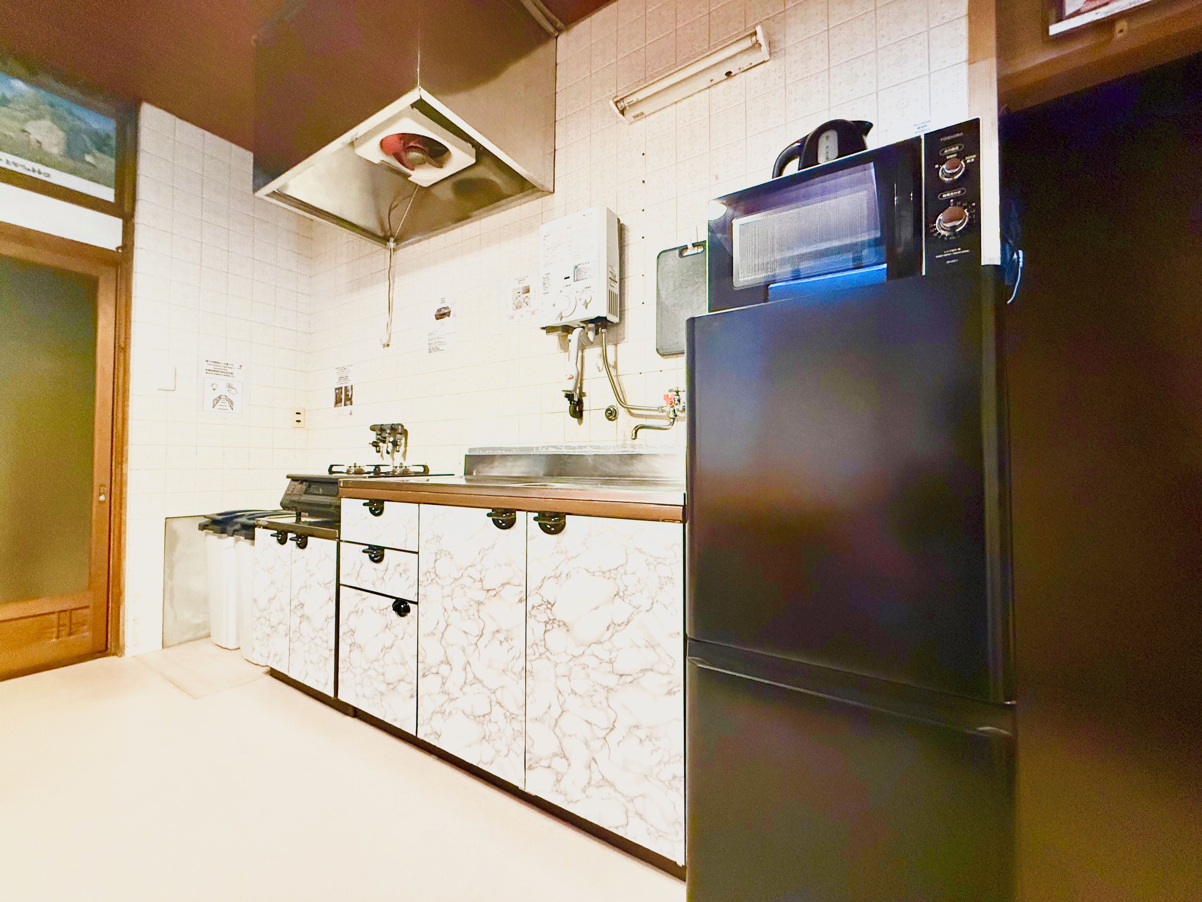 Une cuisine équipée d’un réfrigérateur, d’une cuisinière, d’un four à micro-ondes et d’un plan de travail recouvert de carreaux.