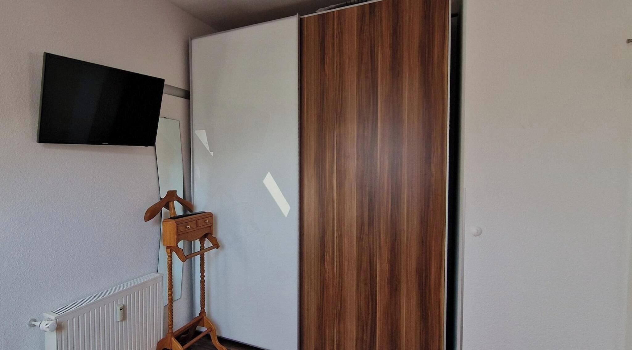 Une pièce avec un radiateur blanc, un porte-manteau en bois et une porte coulissante dotée d’un panneau en bois.