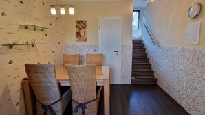 Un área de comedor con sillas de mimbre y una mesa, una escalera con pared de piedra, y un reloj en la pared.