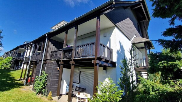 Un edificio de varios pisos con balcones, un área de estar al aire libre cubierta y un jardín bien cuidado.