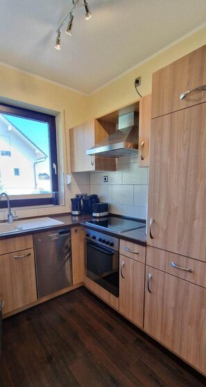 A modern kitchen with wooden cabinets, stainless steel appliances, and a window providing natural light.