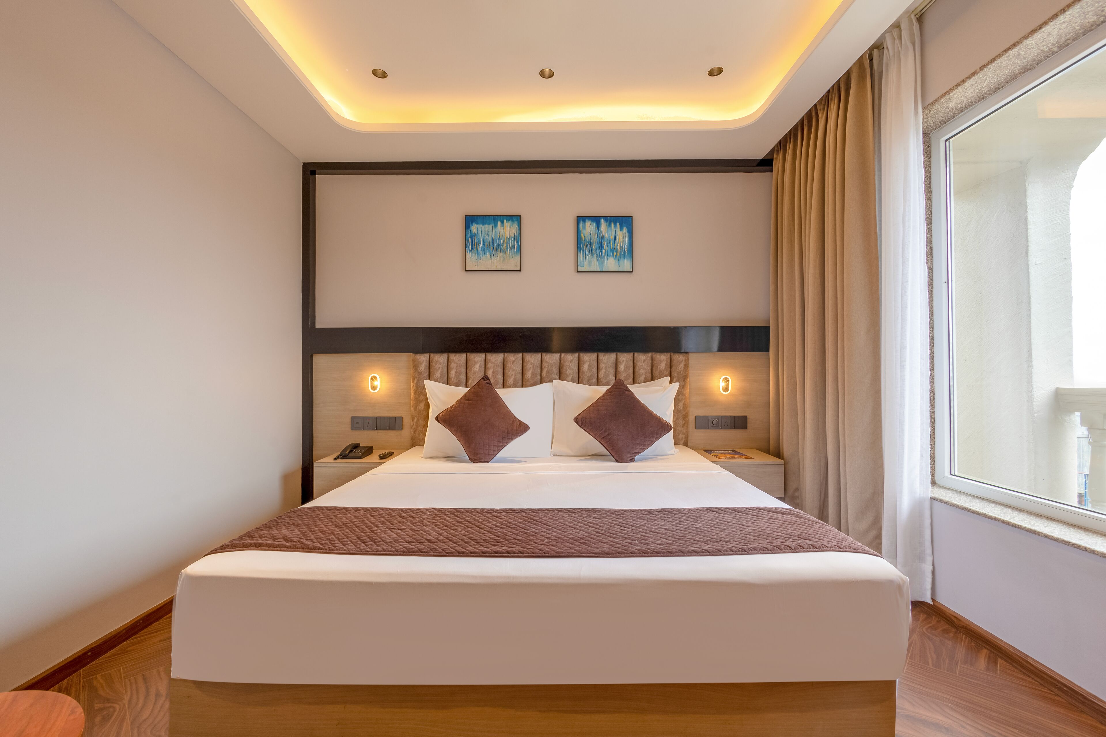 Una habitación de hotel moderna con una cama grande, lámparas de noche y vistas de la ciudad a través de un amplio ventanal.