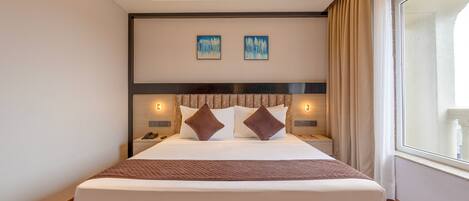 Ein modernes Hotelzimmer mit einem großen Bett, Nachttischlampen und Blick auf die Stadt durch ein großes Fenster.