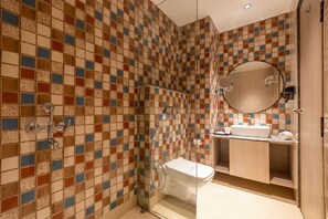 A bathroom with a tiled shower wall, a toilet, a sink, and a mirror.