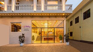 L’entrée d’un hôtel avec une façade en verre, une enseigne indiquant « Sterling Rampath Ayodhya », et des plantes en pot disposées sur le trottoir.