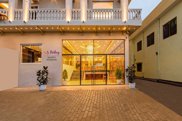 A hotel entrance with a glass facade, a signboard, and potted plants.