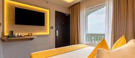 A hotel room with a large bed, a mounted TV, a window with curtains, and a balcony view.