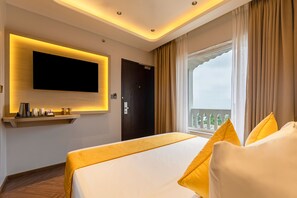 A hotel room with a large bed, a mounted TV, a window with curtains, and a balcony view.