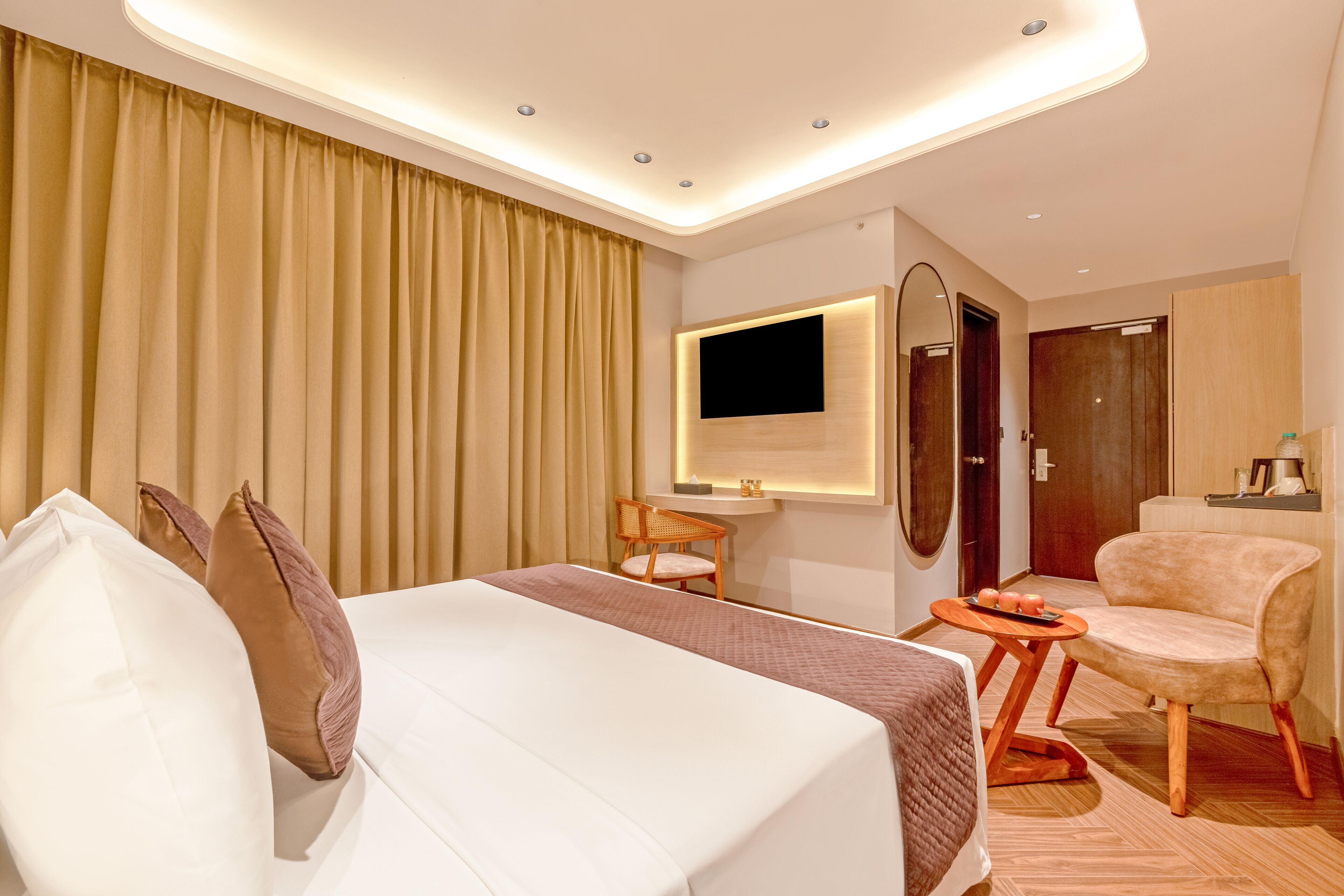 Ein Hotelzimmer mit einem großen Bett, einem Schreibtisch mit Stuhl, einem an der Wand befestigten Fernseher und Holzboden.
